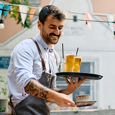Happy waiter serving drinks to group of guests in a cafe.